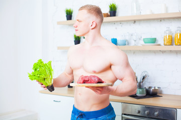 Muscular man with a naked torso in the kitchen with a salad and a piece of beef meat, the concept of a healthy diet. Athletic way of life.