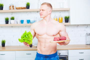 Muscular man with a naked torso in the kitchen with a salad and a piece of beef meat, the concept of a healthy diet. Athletic way of life.