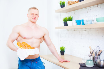 Muscular man with a naked torso in the kitchen with bread, concept of healthy eating. Athletic way of life.