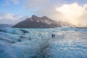 Two people walking on a glacier in Iceland surrounded by mountains