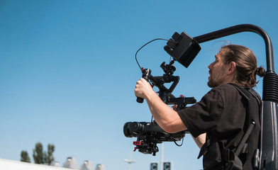 Professional videographer holding camera on 3-axis gimbal which mounted on easy rig. Videographer...