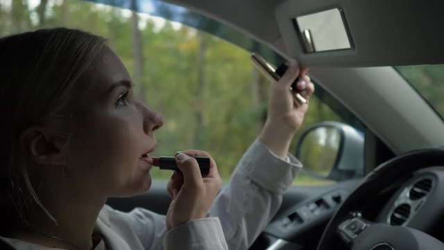 Young blond woman paints her lips in the car.