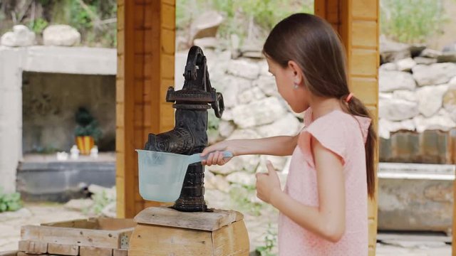 A young girl draws water from a water inlet column. The girl shakes the water.