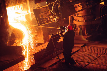 Plant for the production of steel. An electric melting furnace. Factory worker takes a sample for metal.