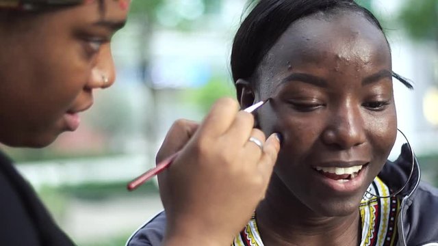 African american black woman is having her makeup done outdoors by a talented make up artist Behind the scenes shot before photo shoot tribal paint themed