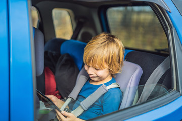 Little boy traveling on backseat of a car using touch pad to entertain himself during the trip