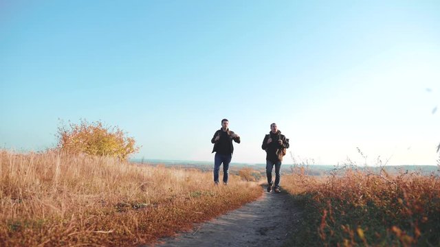 Two men road path traveler hiking with backpacks are walking along the path climbing into the mountains. slow motion video. Tourist Hipster Hiker traveler on background view blue sky clouds go hiking