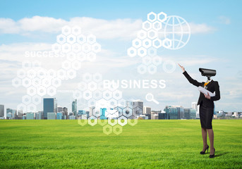 Camera headed woman standing on green grass against modern cityscape