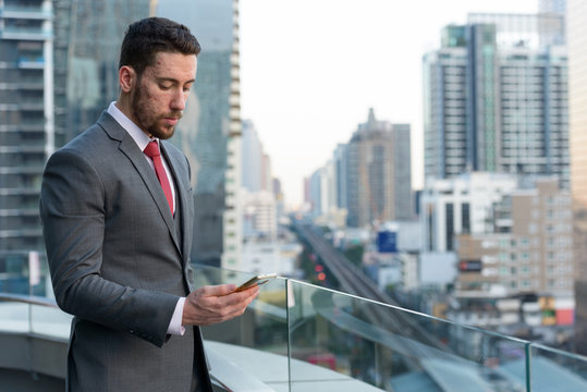 Young handsome Caucasian businessman using mobile phone at rooft