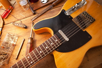 Naklejka premium Guitar on repair desk. Vintage electric guitar on a repair work shop. Single cutaway electric guitar, amber color.