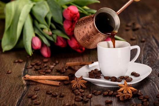 Pouring coffee into a white cup against the background of tulips close up