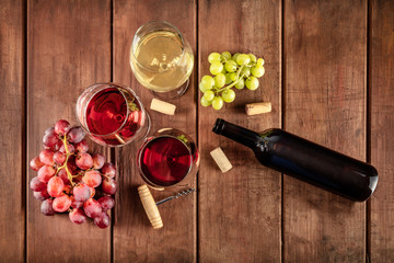 Retro Style Wine Tasting. A photo of glasses of red, rose, and white wine with a bottle, grapes, and a vintage corkscew and corks, shot from above on a dark rustic wooden background with a place for
