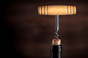 A closeup photo of a vintage corkscrew pulling a cork from a bottle of wine on a dark background with copy space