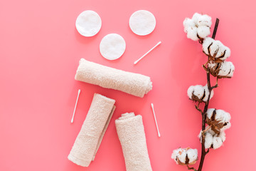 Cotton hygiene products. Cotton pads and swabs, towels twisted coil near dry cotton flowers on pink background top view copy space