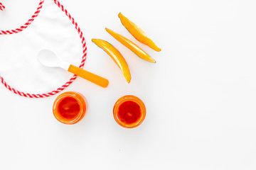 Baby food concept. Pumpkin puree in bowl near bib, pumpkin slices, spoon on white background top view copy space
