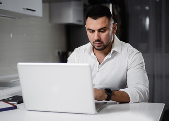 man in white shirt websurfing with laptop in home kitchen