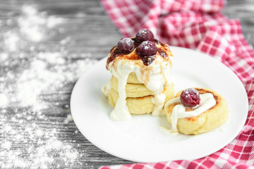 Cottage cheese pancakes with strawberry jam on white plate on grey wooden background. Healthy breakfast.