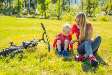 The boy fell off the bicycle, his mother pastes a plaster on his knee