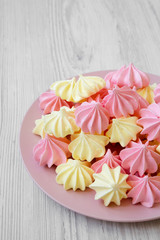 Mini meringues on pink plate over white wooden background, low angle view. Closeup.