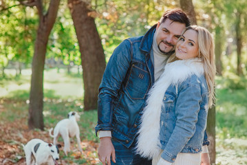 beautiful lovely young couple (woman and man) in jeans clothes walking with two whippet dogs outdoor in autumn (fall) - healthy lifestyle. Pets, love and friendship concept