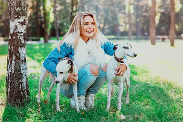 beautiful adorable happy blonde woman owner with her two white whippet outdoor