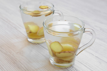 Two mugs of homemade ginger tea with lemon on white wooden surface, side view. Close-up.