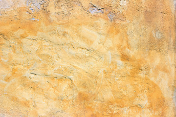 Old yellow painted uneven plaster concrete wall fragment detail background