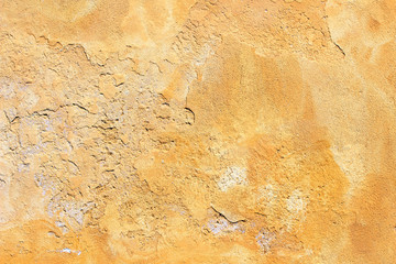 Old yellow painted uneven plaster concrete wall fragment detail background