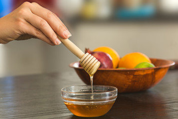 Female hand holding small  wooden honey dipper spoon with small glass bowl with honey.