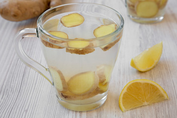 Mug of homemade ginger tea with lemon on white wooden background, side view. Close-up.
