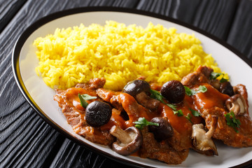 Spanish fricando beef stew with gravy and wild mushrooms served with yellow spicy rice and herbs closeup on a plate. horizontal