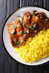 Delicious stewed beef fricando with gravy and wild mushrooms served with yellow rice closeup. Vertical top view