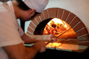Сhef prepares pizza in traditional brick oven.