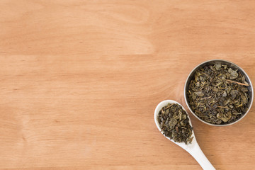 Dry green tea leaves on bowl and ceramic spoon.