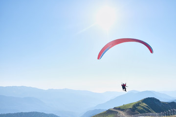 Parachute with two people soars in the clear sky over the magnificent mountain landscape. Non-urban scene. Travel destination. Sports activities.