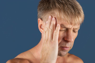 Fototapeta premium A man holds his hands on his head on blue background. Headache or migraine.