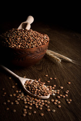 Lentil in a wooden bowl on a wooden background near the ears of wheat. wooden spoon with Lentil