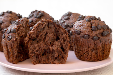 Chocolate cupcakes on pink plate on white wooden table, side view. Close-up.