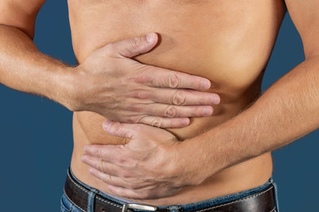 Man holding his stomach in pain. Man with naked torso experience stomachaches on blue background. Medical concept