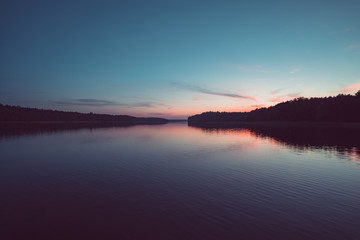 Calm lake with sunset and forest reflection. Peaceful summer evening. 