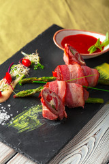 Asparagus rolled in grilled bacon served with sauce on dark plate