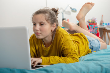 teenager girl lying on the bed, using laptop