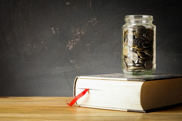 EDUCATION FUND CONCEPT with coins in a glass jar and old book.