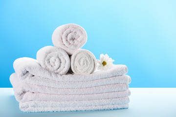 Obraz na płótnie Canvas rolled and stacked towels with beautiful white chamomile flower on blue