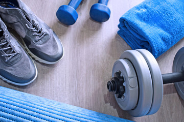 Sneakers, two blue dumbbells, a towel and a workout mat. Sport fitness items on light grey wooden background with empty text space. Active lifestyle, weight loss, body care concept. Top view.