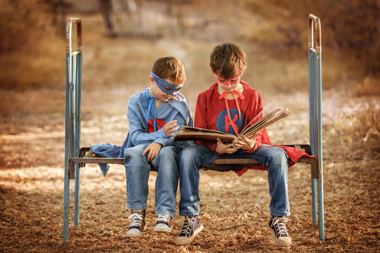Two boys dressed as a superhero looking photo album in a garden