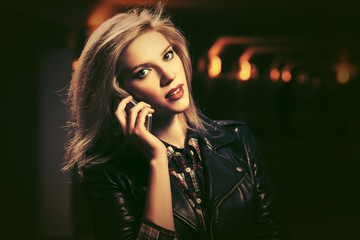 Naklejka premium Young fashion blond woman in leather jacket talking on cell phone