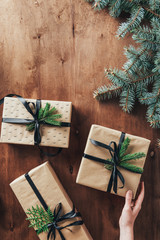 cropped view of woman touching gift boxes on wooden background with christmas tree branches