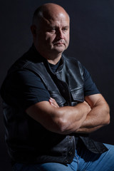 Adult brutal bald man in a leather jacket, dark background