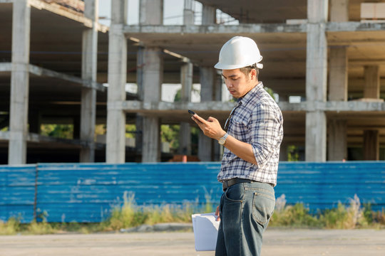 Young engineer in safety engineer helmet using cell phone or texting at the construction site.